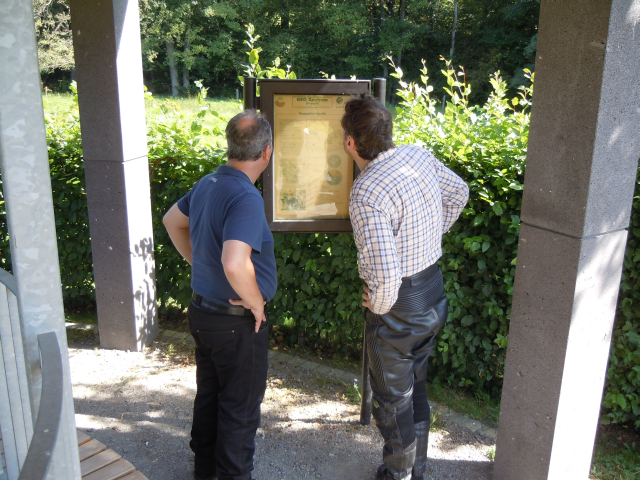 Andreas und H.J. stehen an der Info ueber den Duppacher Drees - eine oeffentliche Mineralquelle 